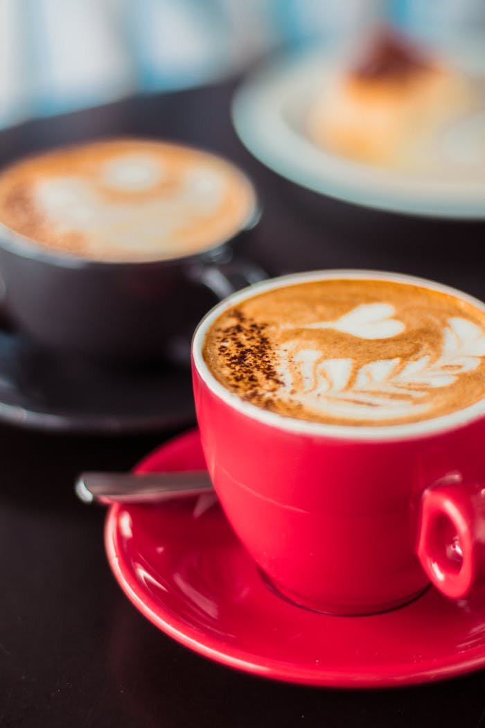 Two coffee cups with intricate latte art designs sitting on a table, highlighting barista skills.