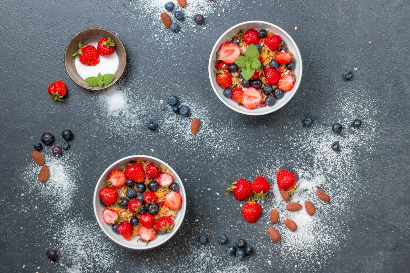 Top view of fresh berry and almond bowls with sugar on dark slate.